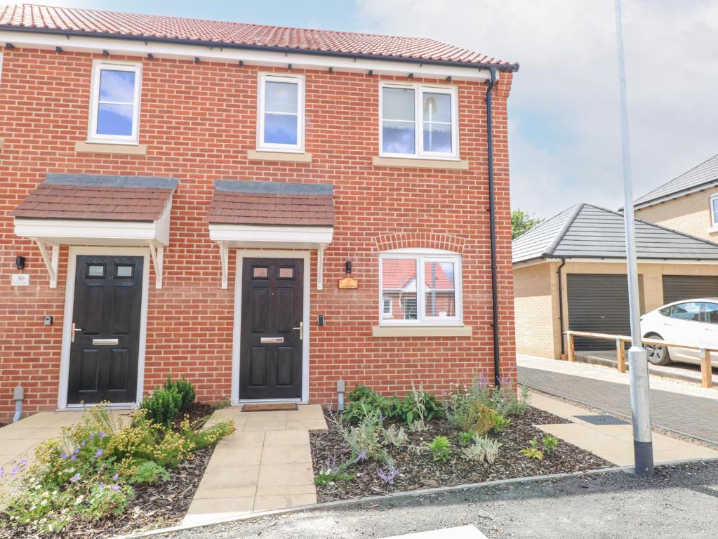 a brick house with black doors on a street at Pine Cottage in Beccles