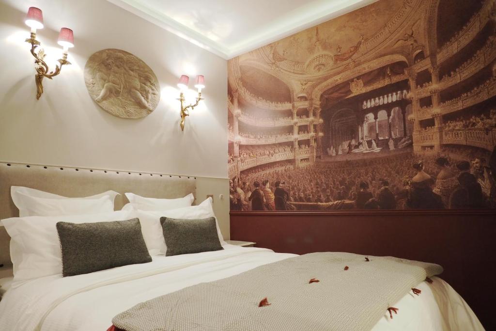パリにあるパレ ロワイヤル シックスイーツのベッド付きの客室で、壁には絵画が飾られています。