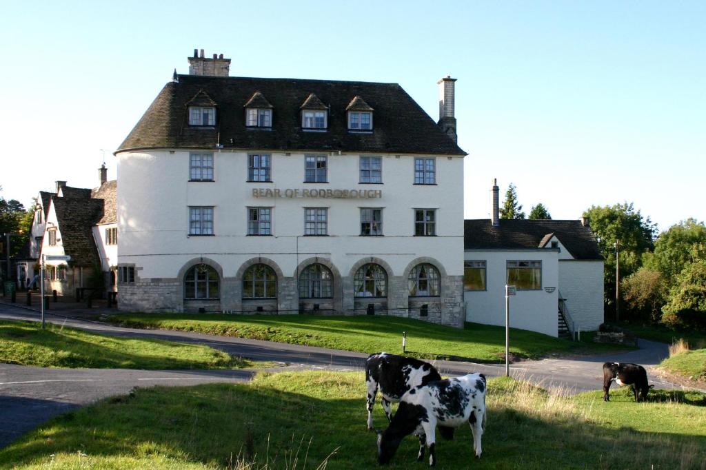 a black and white cow standing in front of a white house at The Bear Of Rodborough Hotel in Stroud