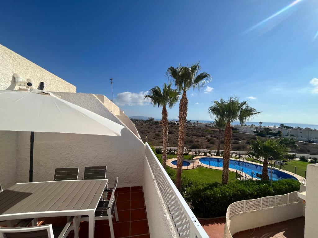a balcony with a table and an umbrella and a pool at Los cántaros Apartamento Mojácar in Mojácar