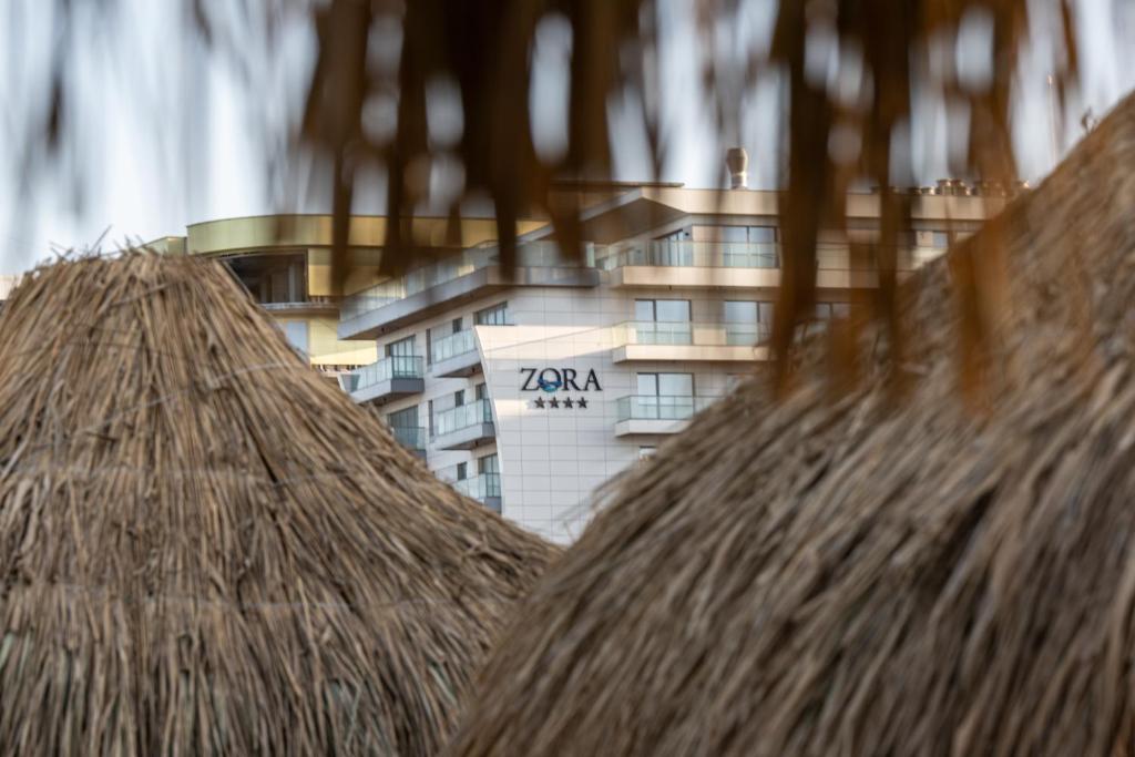 a building in the background with a straw roof at L&C Beach Home by Zora apartament,pe plaja in Mamaia Nord