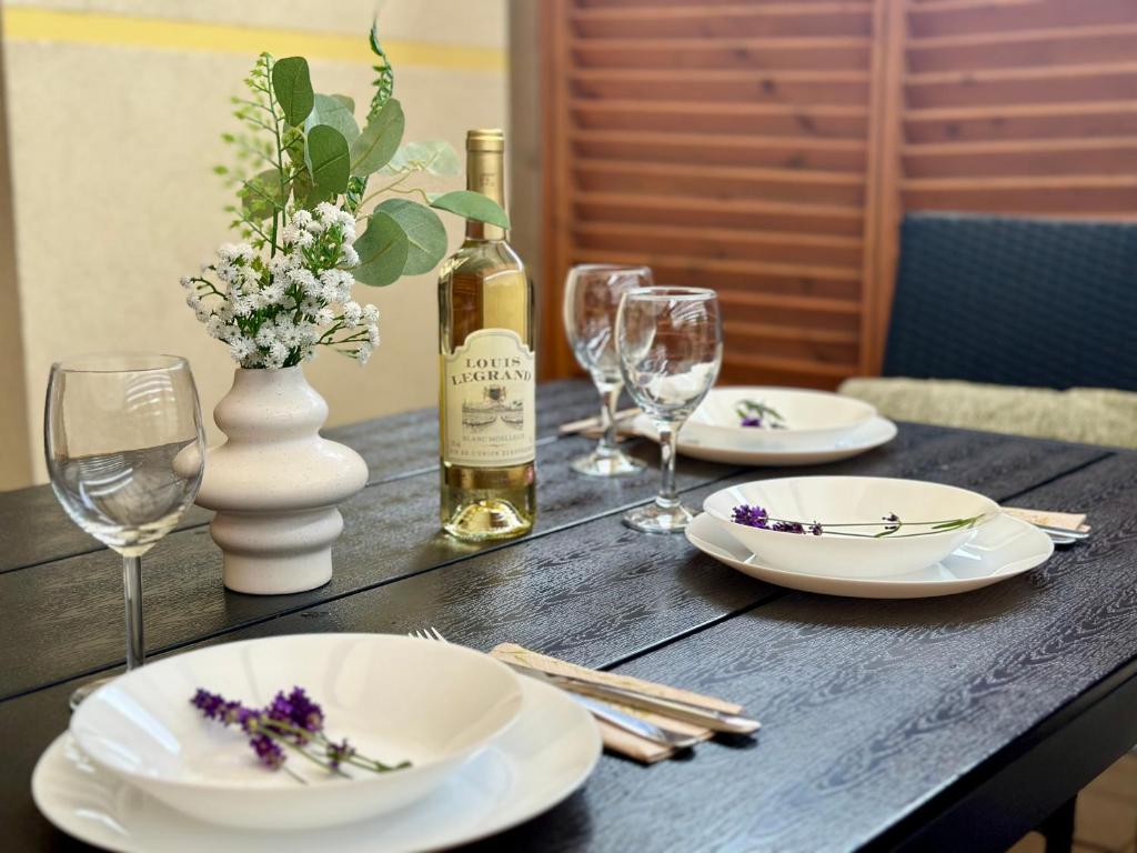 Place settings with white plates, wine glasses, bottle of Louis Legrand and floral vase.