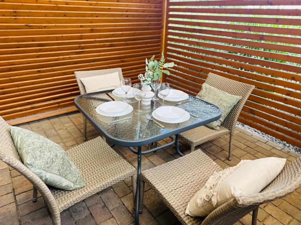 Wicker patio dining set around glass table, place settings and cushions against wooden slatted privacy wall.