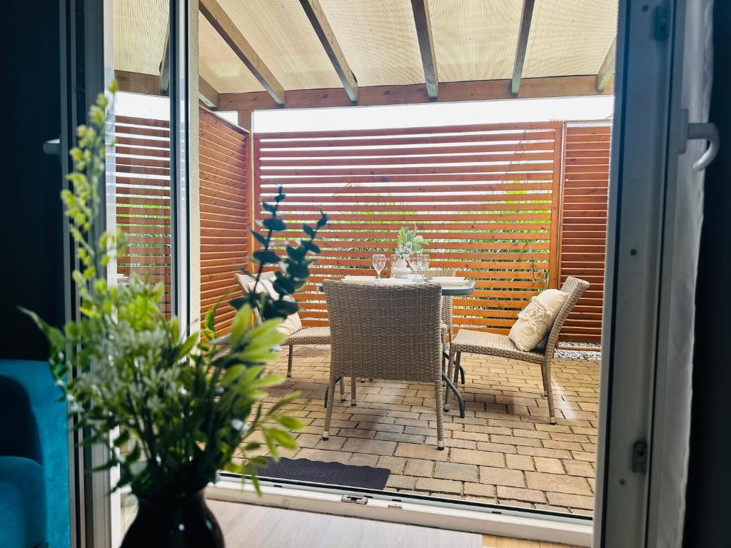 View through open doorway to patio dining set, foreground leafy plant framing scene.