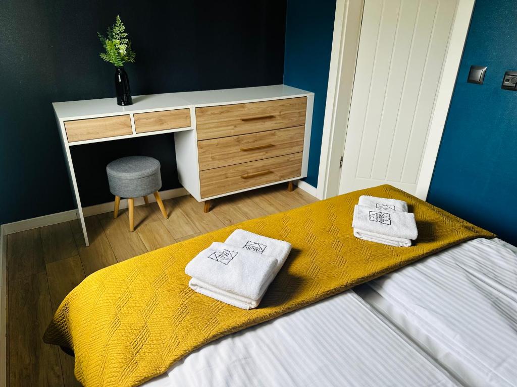 Bright bedroom with mustard bed runner, neatly folded towels and wooden desk against blue wall
