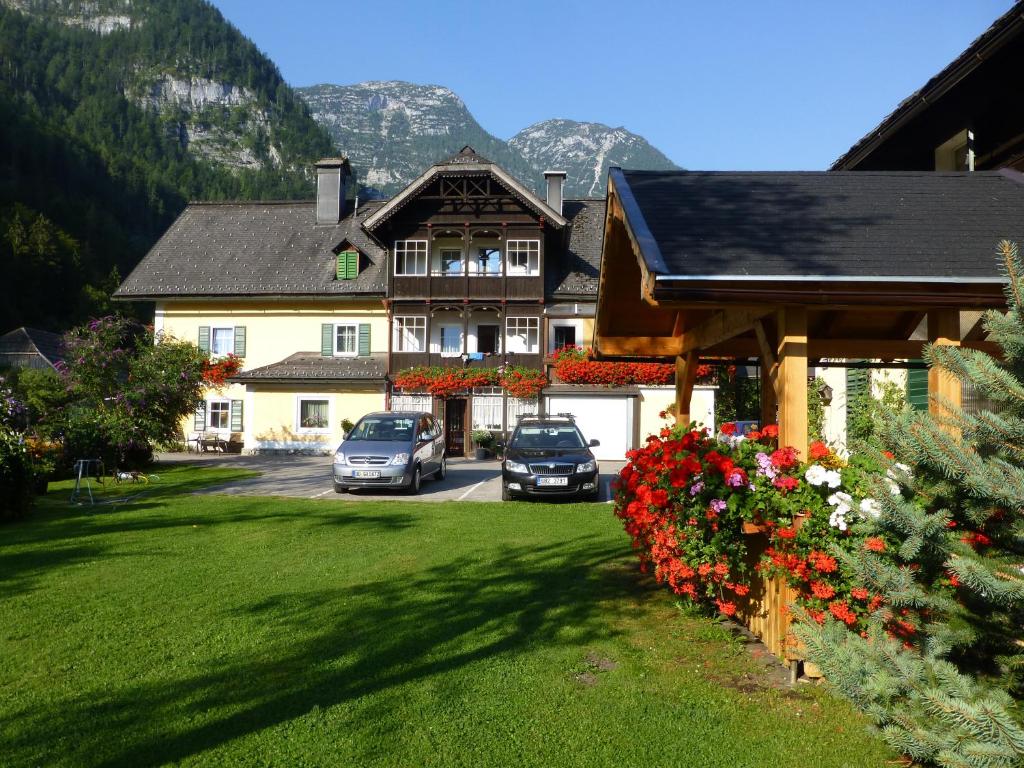 ein Haus mit Autos auf einem Hof mit Blumen in der Unterkunft Gästehaus Binder in Obertraun