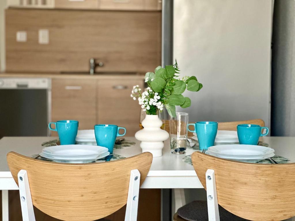 Casual dining table set with turquoise mugs, white plates and central vase of greenery