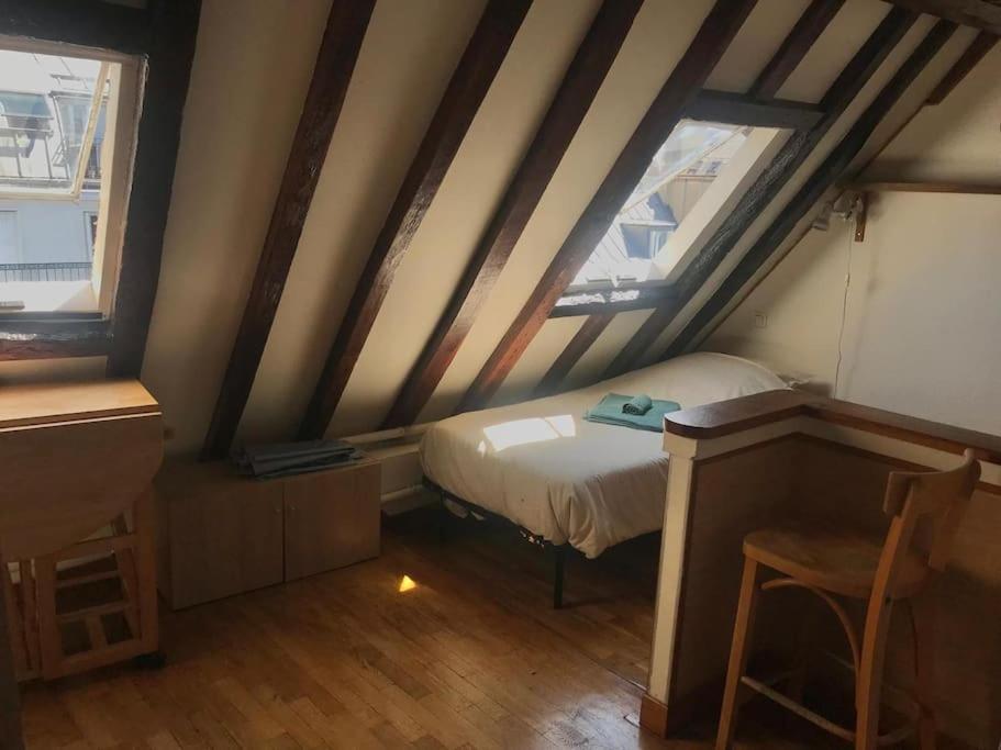 Cette petite chambre mansardée comprend un lit et deux fenêtres. dans l'établissement Studio parisien plein de charme, à Paris