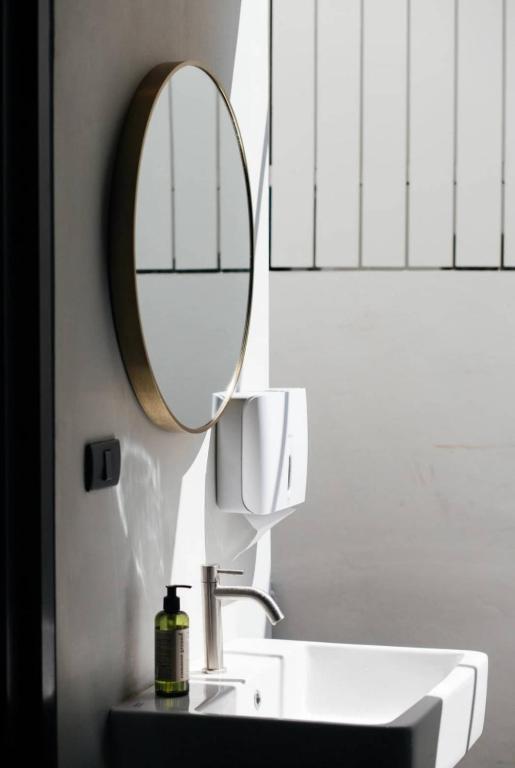 A compact vanity with a round mirror, basin, soap, and wall-mounted hairdryer.