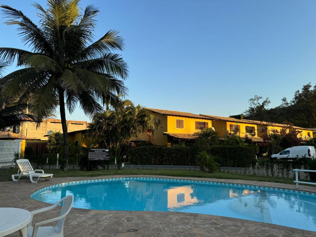 a swimming pool with a palm tree and a building at Casa em Condomínio de Búzios com Vista para o Mar in Búzios