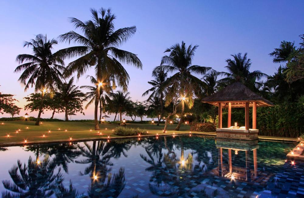 uma piscina à noite com palmeiras e um gazebo em Villa Hanani em Jimbaran