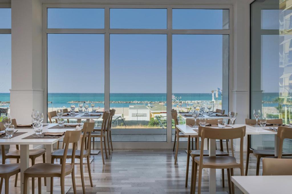 a restaurant with tables and chairs and large windows at Hotel Aqua in Cattolica