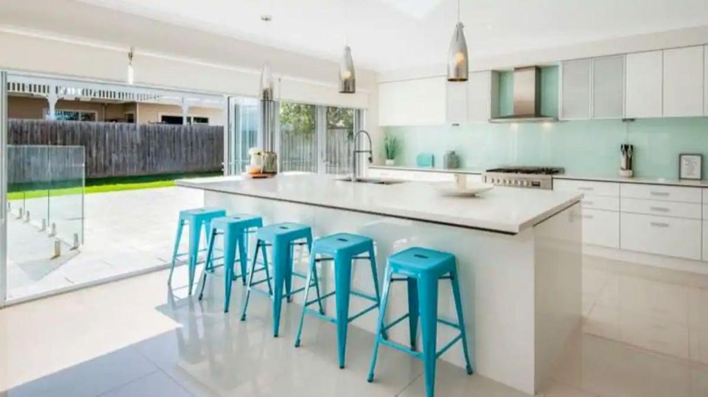 a kitchen with a island with four blue stools at Seachange Family Escape with Pool and Spa Bath in Saint Leonards