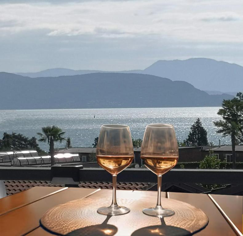 two wine glasses sitting on a table with a view of the ocean at Note di lago in Manerba del Garda