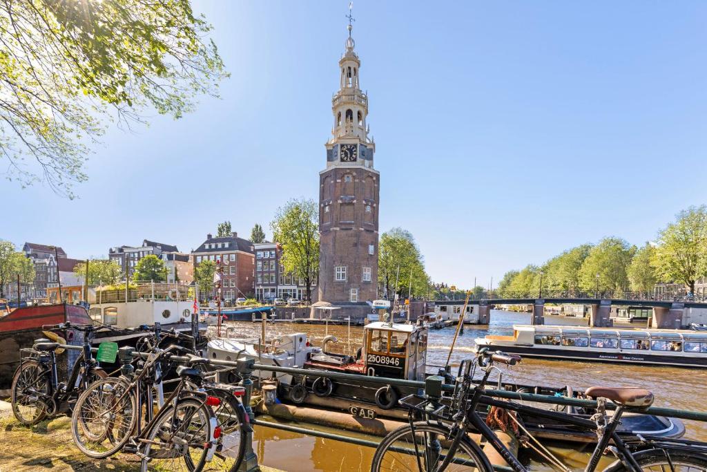 アムステルダムにあるCentral Art Apartment - Nieuwmarkt areaの時計塔のある川のそばに駐車された自転車の群れ