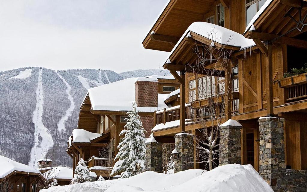 a building covered in snow with mountains in the background at Ski in Ski out 4 Bedroom Spruce Peak Lodge Luxury Mountain Cabin By Stowe Mountain Rentals in Stowe