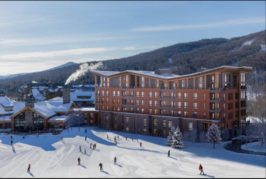 a group of people skiing in the snow in front of a building at 4F One Spruce Peak Stowe Mountain Resort Ski in Ski Out 4 bed Sleeps 10 in Stowe