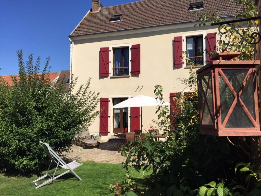 une maison avec volets rouges et parasol dans la cour dans l'établissement Gite Les Volets Rouges, à Vigny