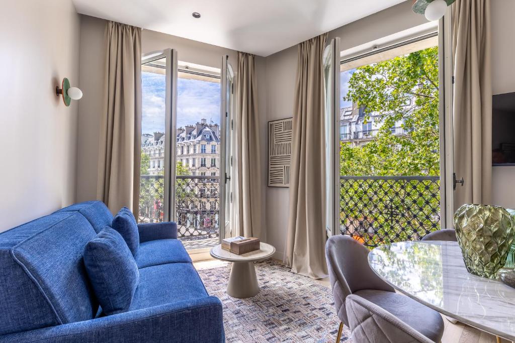 un salon avec un canapé bleu et une grande fenêtre dans l'établissement Quartier Libre Marais, à Paris