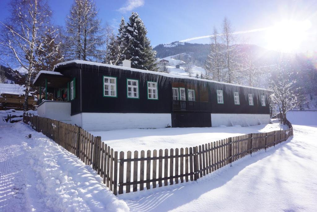 a black house with a fence in the snow at Ferienhütte mit Außensauna in Grossarl