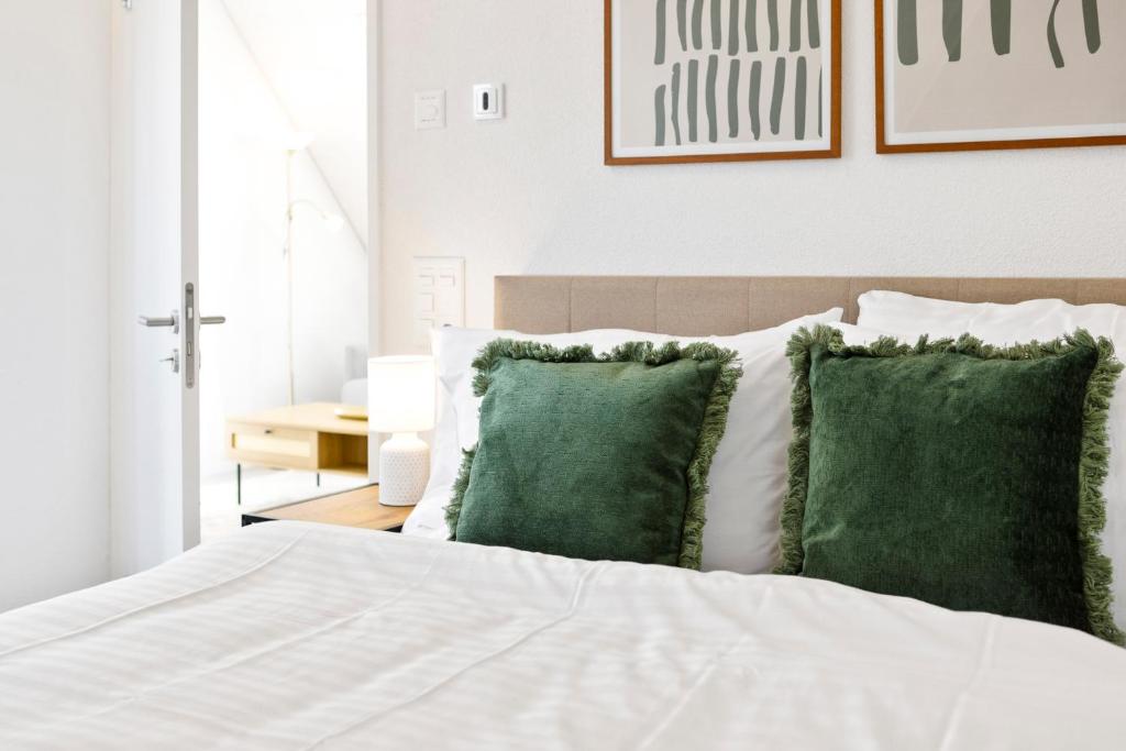 a bedroom with a white bed with green pillows at STAYY Flagship Limmattal - contactless check-in in Schlieren