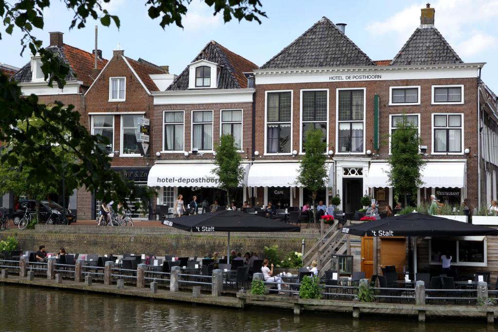 a building with tables and umbrellas next to a river at Hotel Café Restaurant De Posthoorn in Dokkum