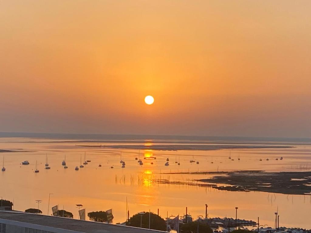 un coucher de soleil sur une étendue d'eau avec des bateaux dans l'établissement Aux pieds des plages, du port, de la piste cyclable et des commerces de proximité, un studio au dernier étage avec une vue panoramique sur le Bassin d'Arcachon, entièrement rénové, dans une résidence avec piscine, à Arcachon