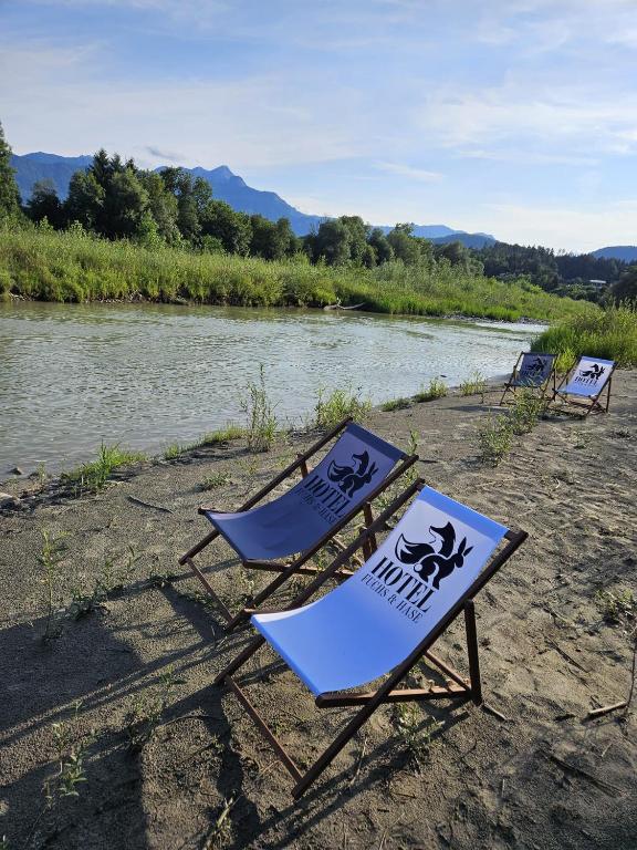 three lawn chairs sitting on a beach next to a river at Hotel Fuchs & Hase SELF CHECK IN in Rosegg