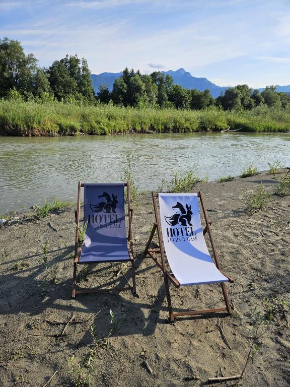 two chairs sitting on a beach next to a river at Hotel Fuchs & Hase SELF CHECK IN in Rosegg