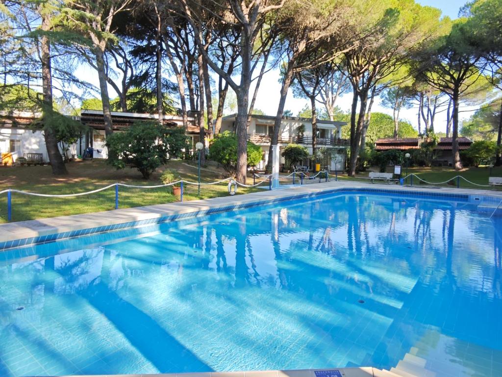 Una gran piscina azul con árboles al fondo. en Villa DUNA ROMANTICA, en Lignano Sabbiadoro