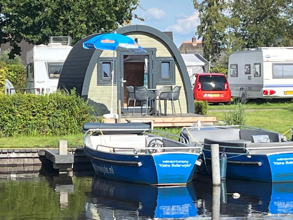 Due barche sono ormeggiate sull'acqua di fronte a una casa di Camping Kleine Belterwijde, Pod, Tiny House aan het water a Belt-Schutsloot