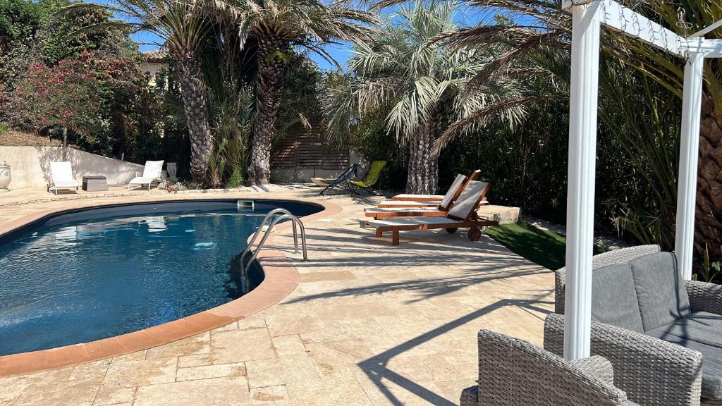 - une piscine avec une chaise, un banc et des palmiers dans l'établissement L'oasis-LES ISSAMBRES, aux Issambres