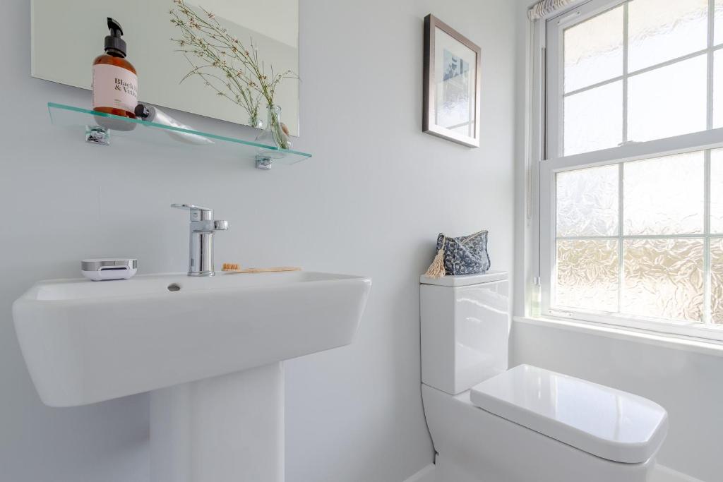 a white bathroom with a sink and a window at Sandpipers, Port Isaac Bay Holidays in Port Isaac