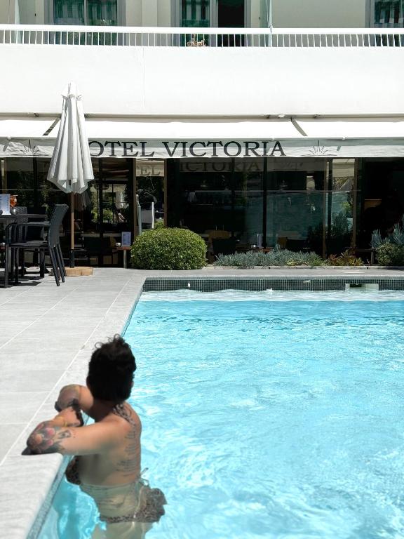 a man in a swimming pool next to a hotel at Hôtel Victoria in Cannes