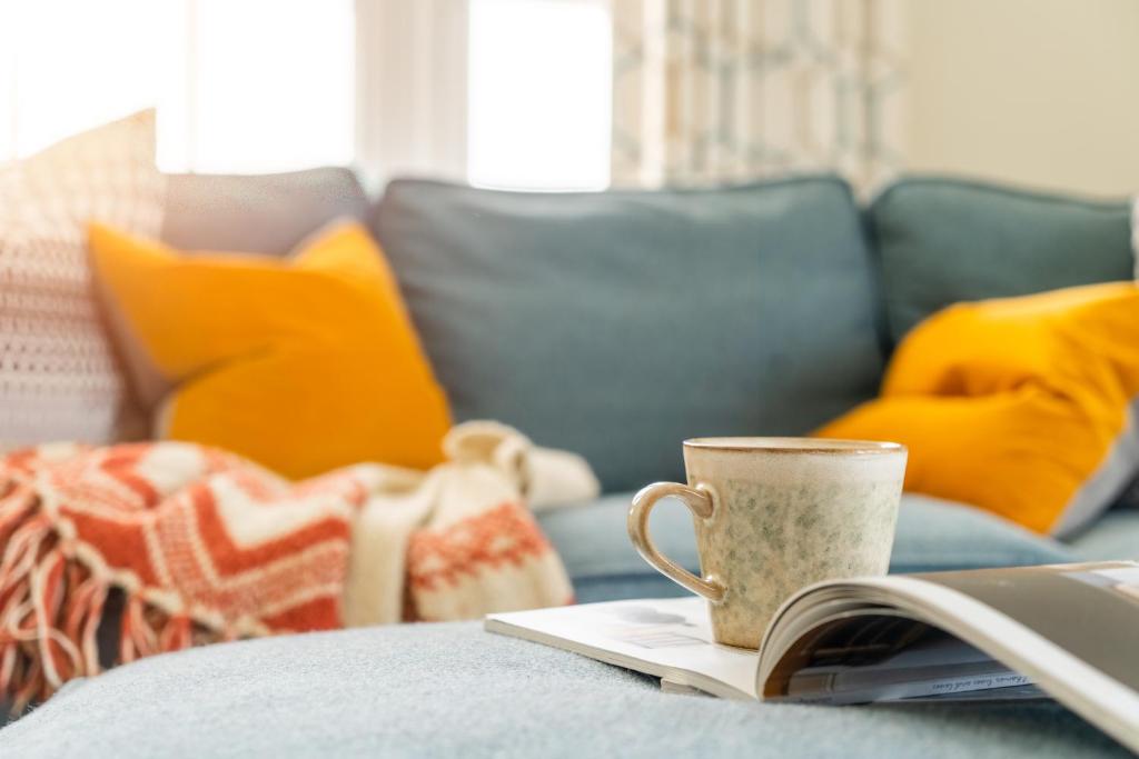 a book and a coffee cup on a couch at Sandpipers, Port Isaac Bay Holidays in Port Isaac