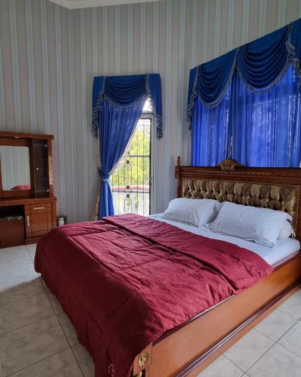 a bedroom with a large red bed with blue curtains at Villa Kota Bunga AA2-11 in Cikundul