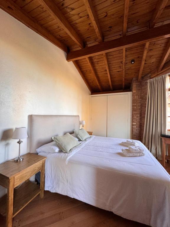 1 dormitorio con 1 cama blanca grande y techo de madera en La Bignonia Posada, en Chacras de Coria