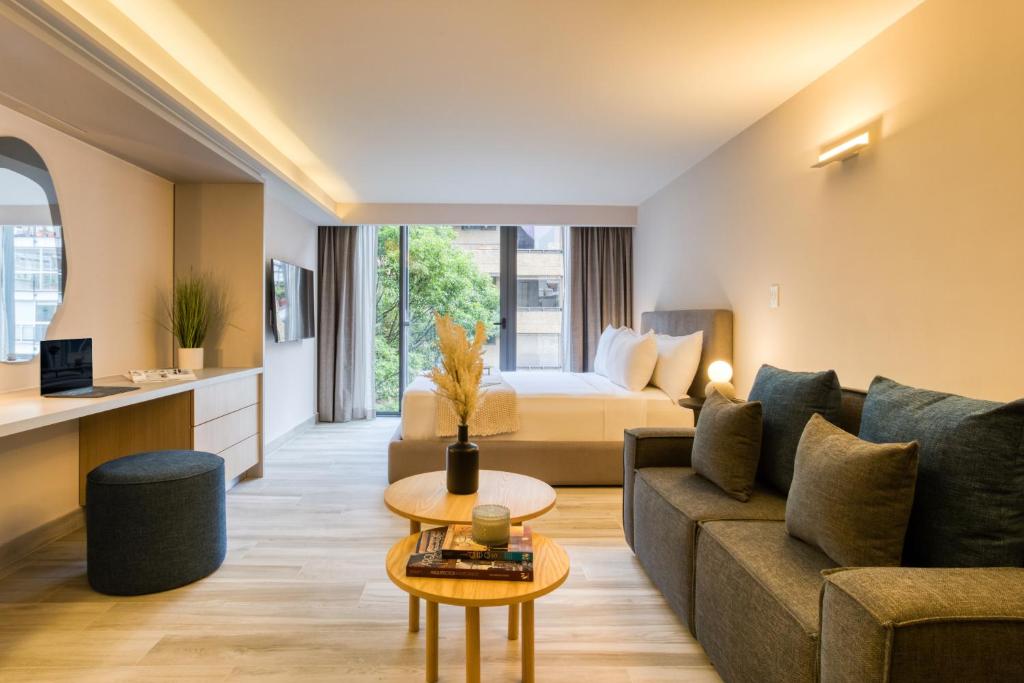 An open-plan apartment room combining a sofa lounge, kitchenette, desk and bed by the window.