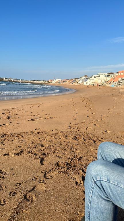a person sitting on a beach with footprints in the sand at Dahomey plage appartement Dahomey city in Bouznika