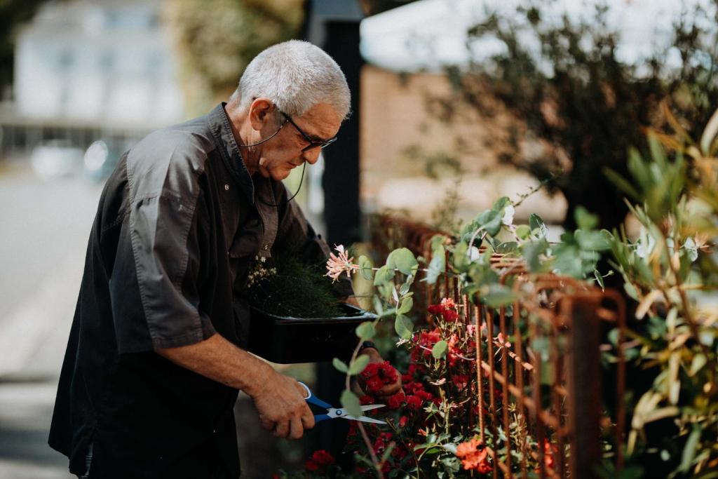 an older man cutting a plant in a garden at Hotel Restaurant Le Cigalon in Waldbillig