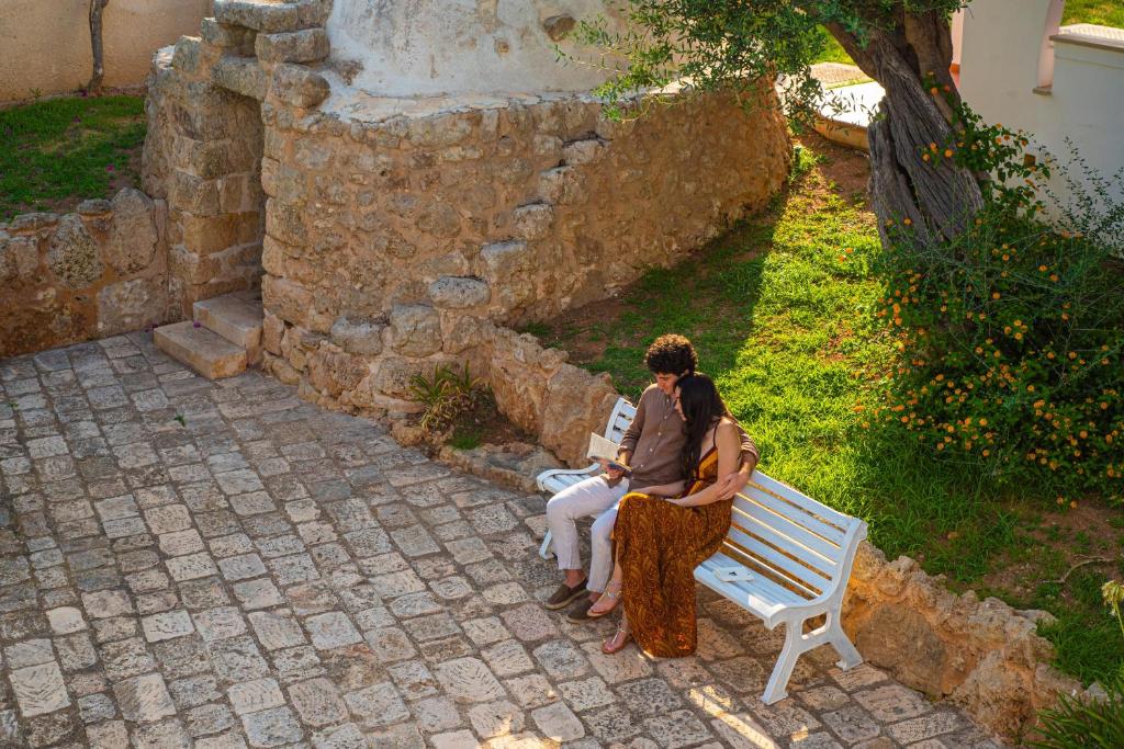 two people sitting on a bench next to a stone wall at Pietrablu Resort & Spa - CDSHotels in Polignano a Mare