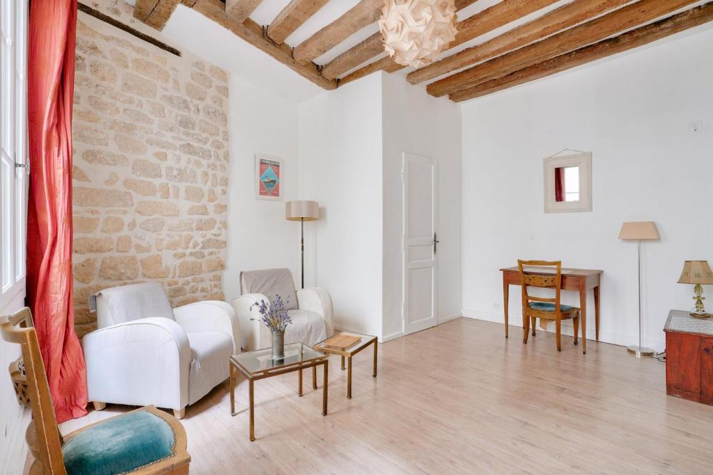 Il comprend un salon doté d'un mobilier blanc et d'un mur en briques. dans l'établissement GuestReady - Charmant Apt pour 2 au Cœur de Paris, à Paris