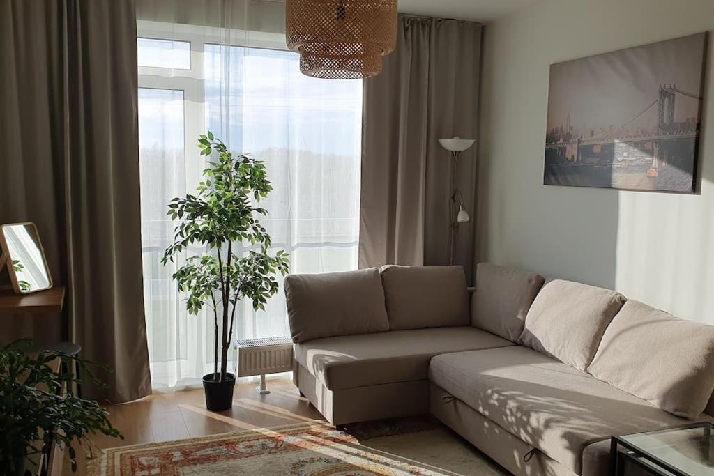Una sala de estar con un sofá y una ventana grande. en Уютная квартира студия в новом проекте в Риге, en Riga