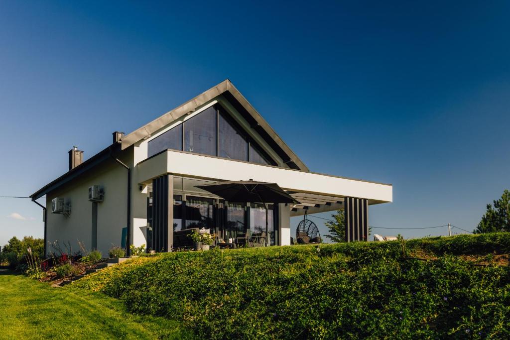 a house on top of a grassy hill at Kalwa Lake House - dom nad jeziorem z prywatnym pomostem i jacuzzi oraz sprzętem wodnym in Pasym