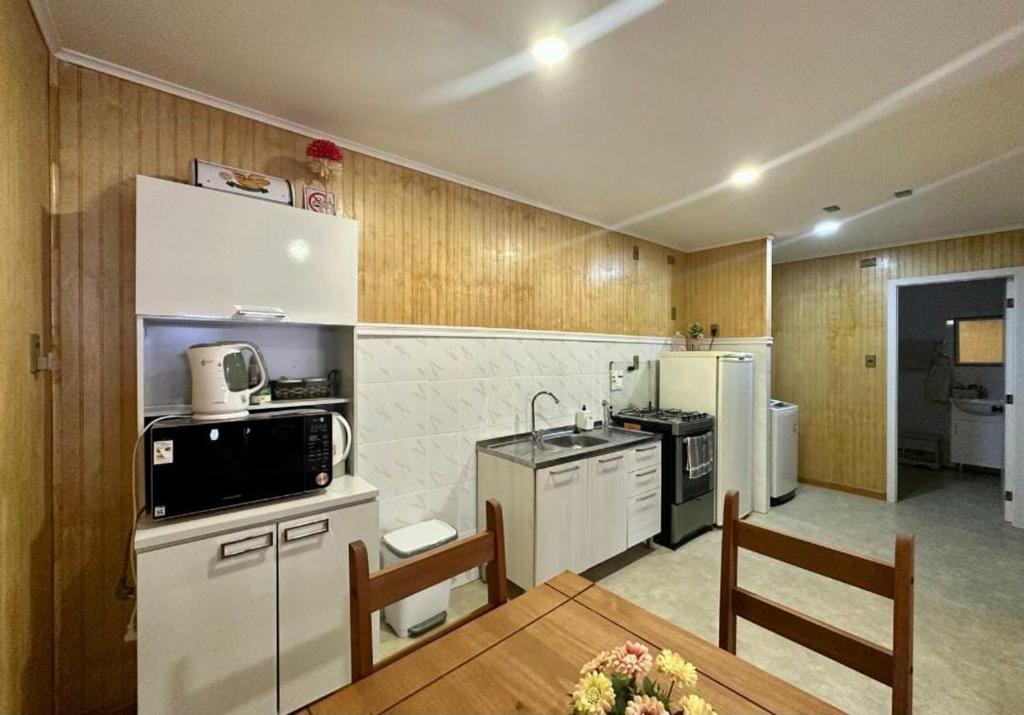 una cocina con electrodomésticos blancos, mesa y sillas en Departamentos Dragones Puerto Natales, en Puerto Natales