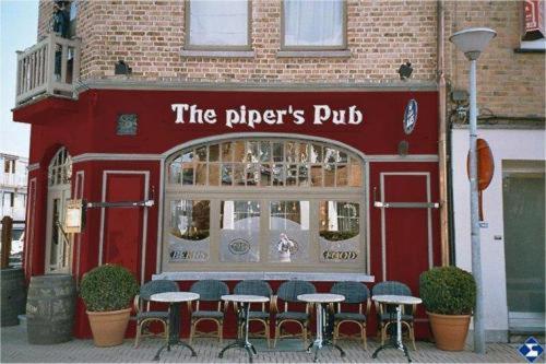 a red building with tables and chairs in front of a restaurant at The Pipers in Middelkerke
