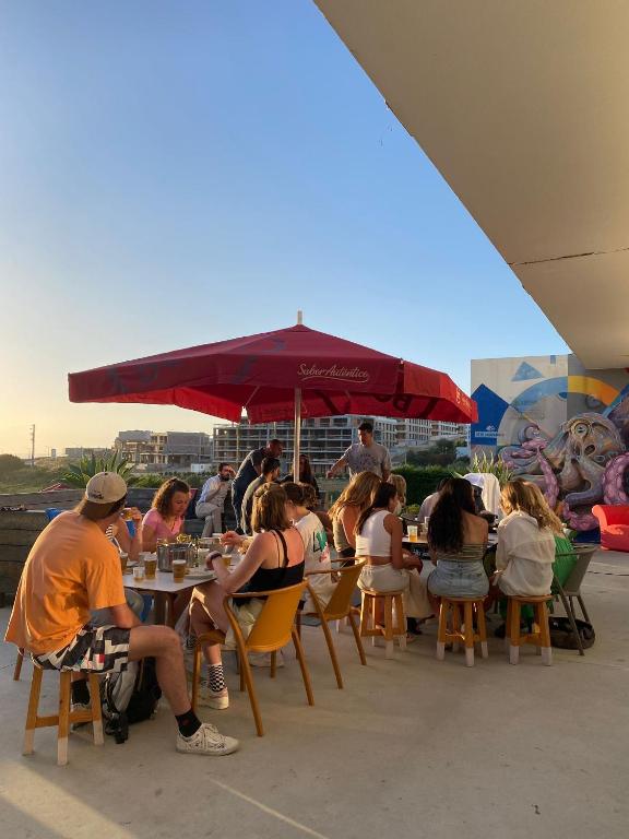 a group of people sitting at tables under an umbrella at WOT Ericeira Surf Hostel in Ericeira
