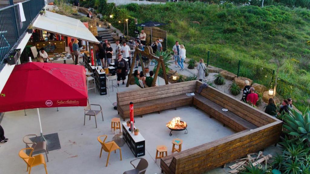 a crowd of people walking around a patio with a fire pit at WOT Ericeira Surf Hostel in Ericeira