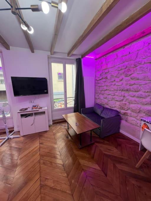 un salon avec des lumières violettes sur un mur en briques dans l'établissement Studio de charme centre paris 10 min de république, à Paris