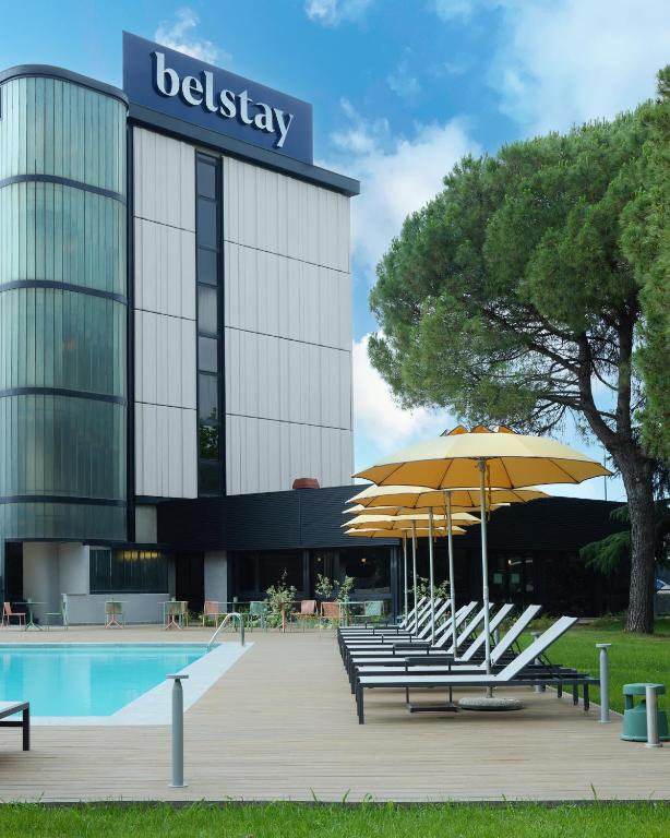 a hotel with benches and umbrellas in front of a pool at Belstay Venezia Mestre in Marghera